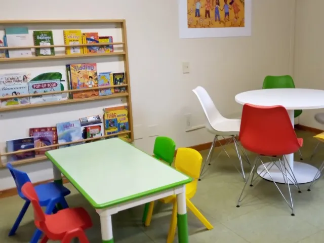 interno con due tavoli con sedie, per bambini e per adulti. Alla parete, una libreria per bambini con libri illustrati