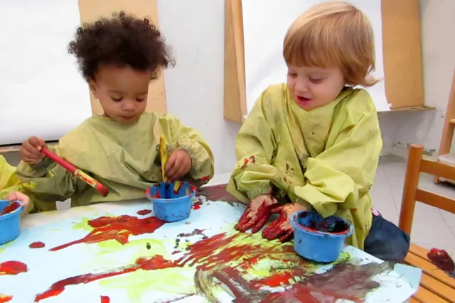 due bambine attorno a un tavolo stendono colori con le mani su un foglio