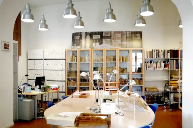 sala con libreria a parete e tavolo centrale dotato di lampade per la consultazione dei materiali archivistici