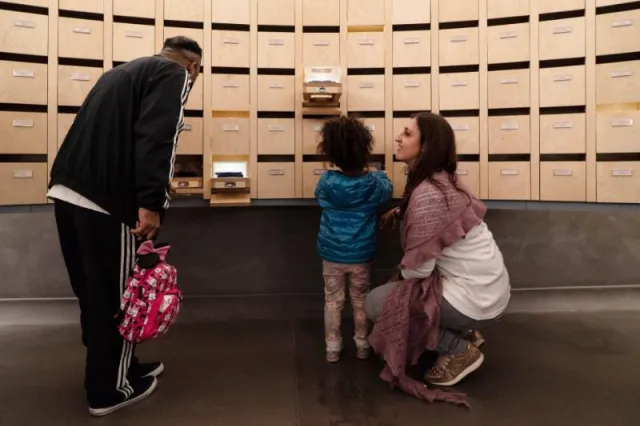 un uomo, una bambina e una donna osservano una sala espositiva del Museo degli Innocenti con cassettini estraibili 