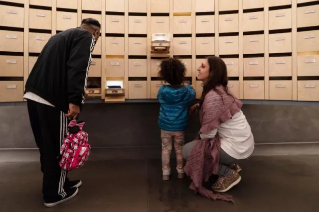 un uomo, una bambina e una donna osservano una sala espositiva del Museo degli Innocenti con cassettini estraibili