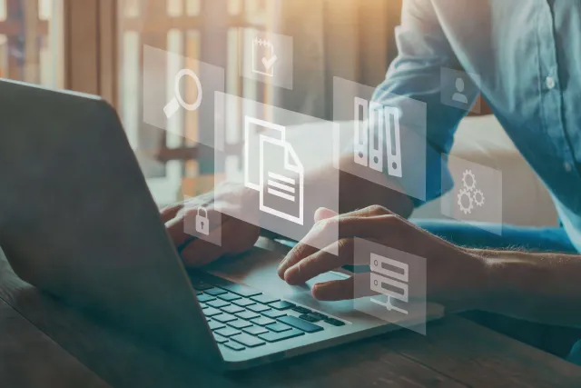 Mani che digitano su un computer portatile. All'immagine si sovrappongono ologrammi con simboli del linguaggio digitale