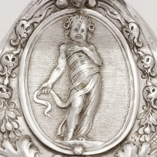 particolare di oggetto liturgico in argento recante una raffigurazione di putto in fasce